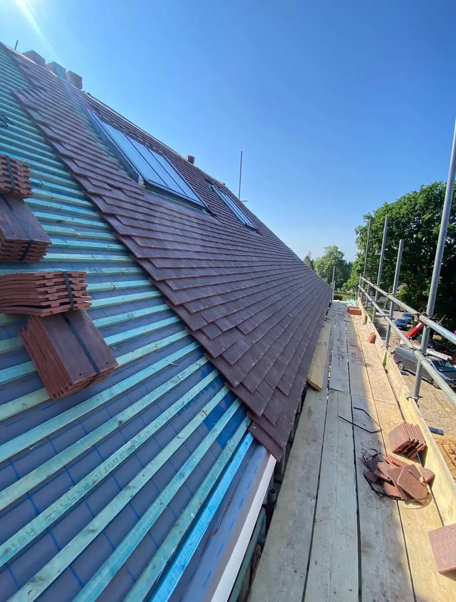 Red tiles going on over blue membrane around a new roof window