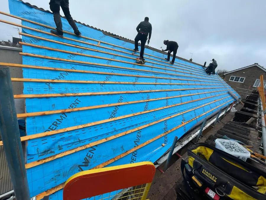 Three roofers on a blue membraned roof fixing battens