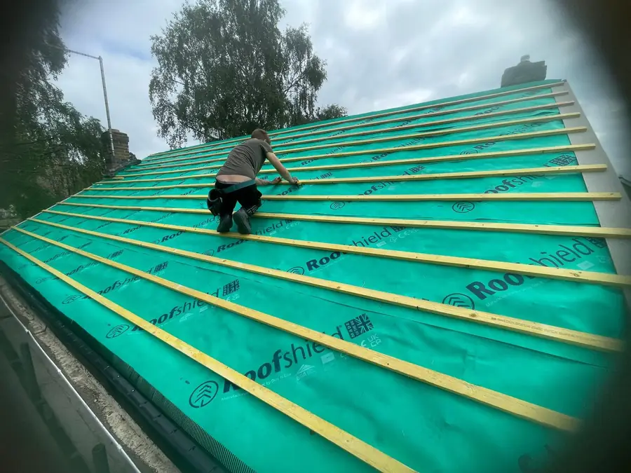 Roofer battening over green membrane on a large pitched roof