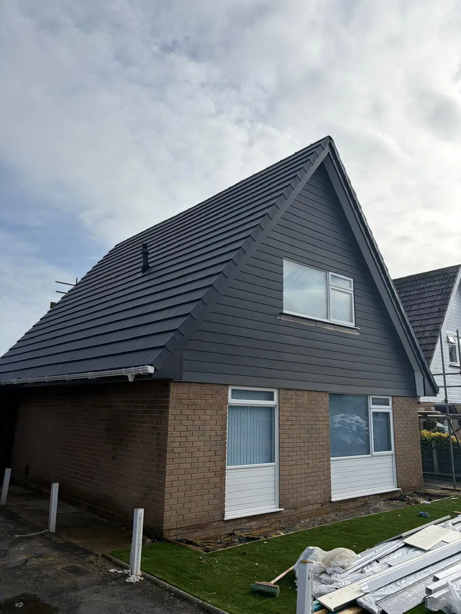 Finished new roof in grey interlocking tiles on a chalet bungalow, scaffold still up