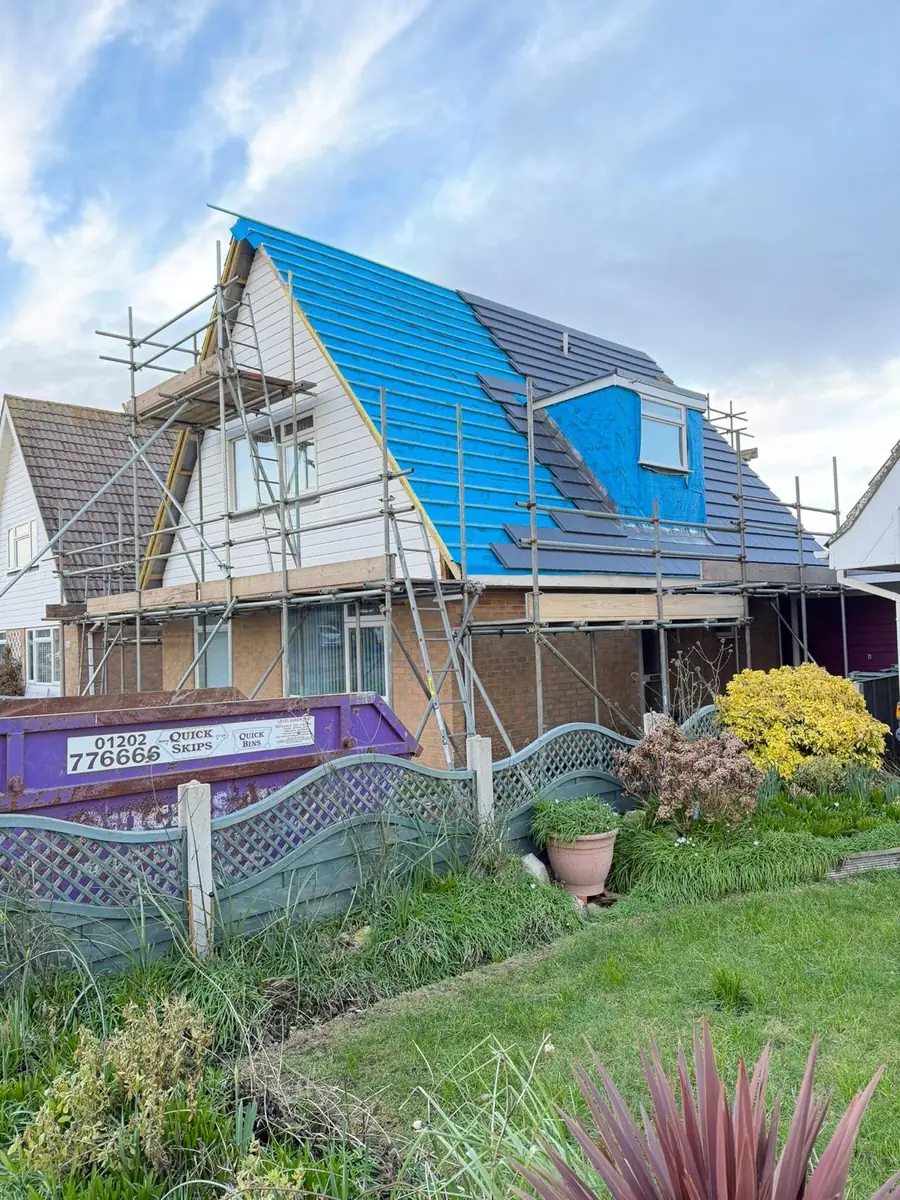 Semi-detached house mid re-roof with blue membrane and scaffold, seen from the garden