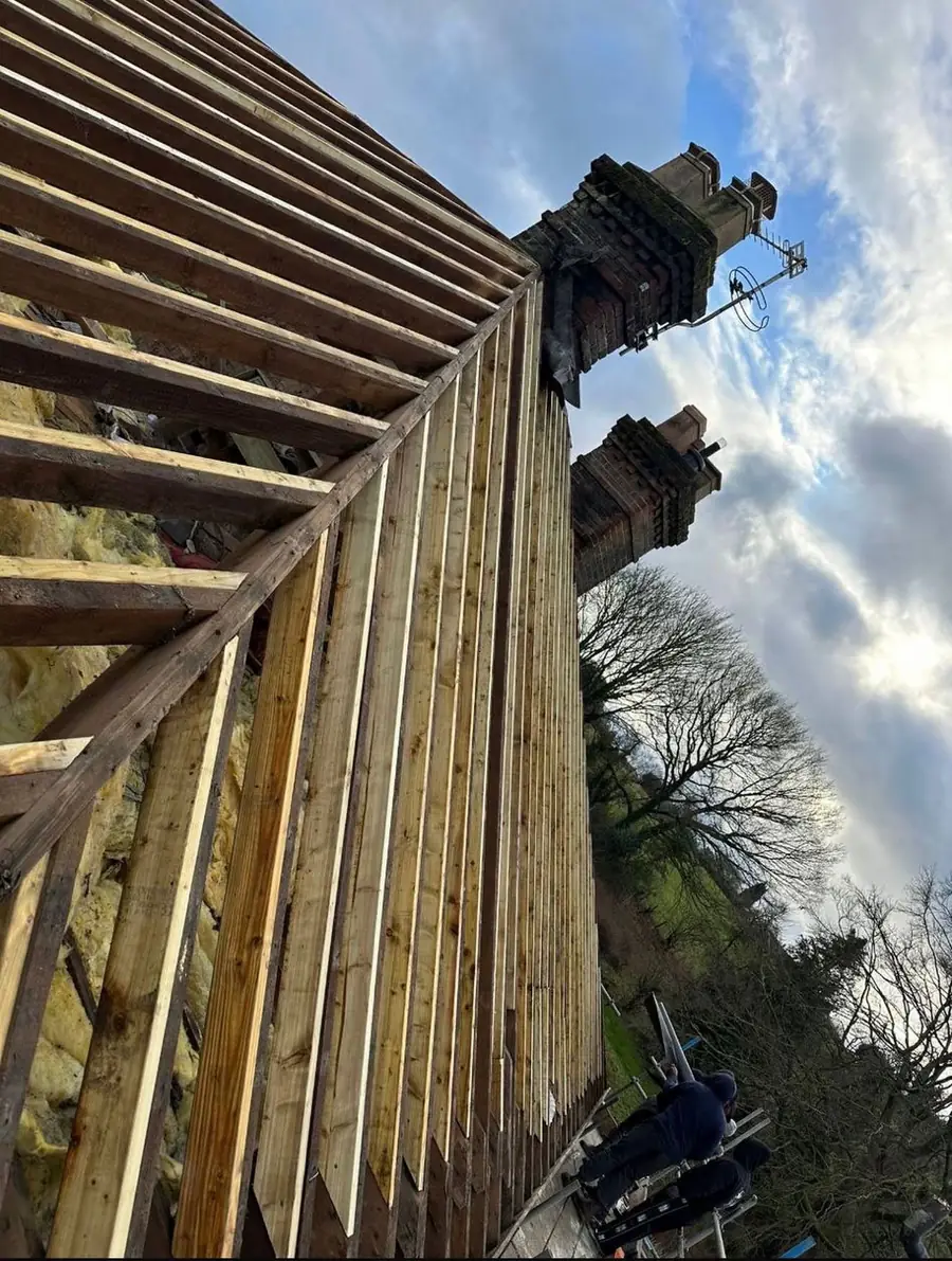 Rafters exposed against the sky during a full strip beside a chimney