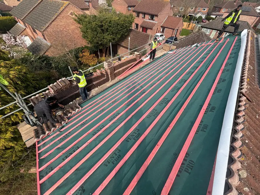 Green breathable membrane and battens going on during a re-roof, team at the ridge