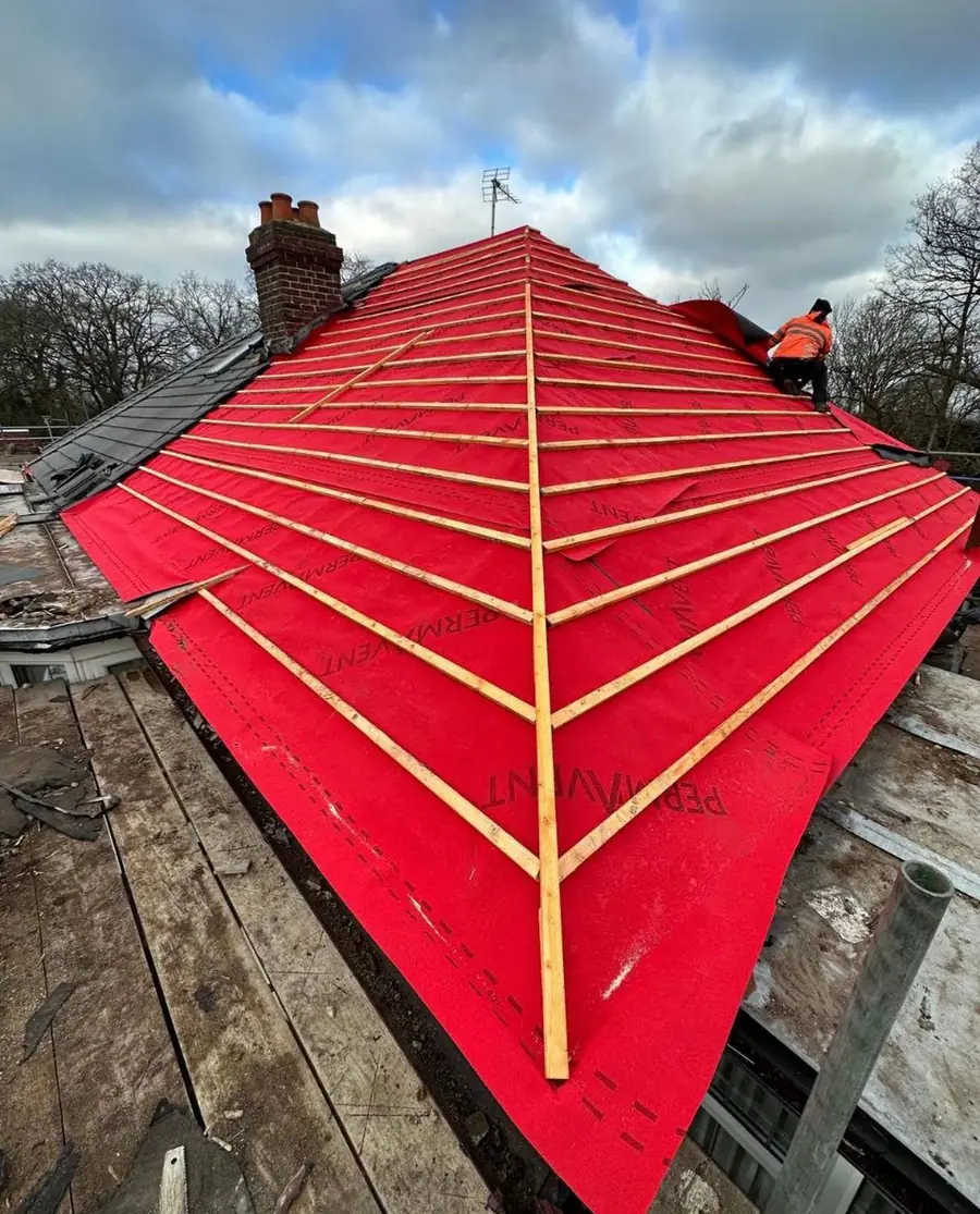 Red breathable membrane and battens on a hipped roof with a roofer at the ridge