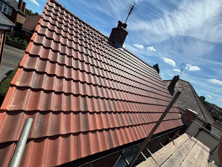 Red interlocking tiled roof with new ridge beside a chimney