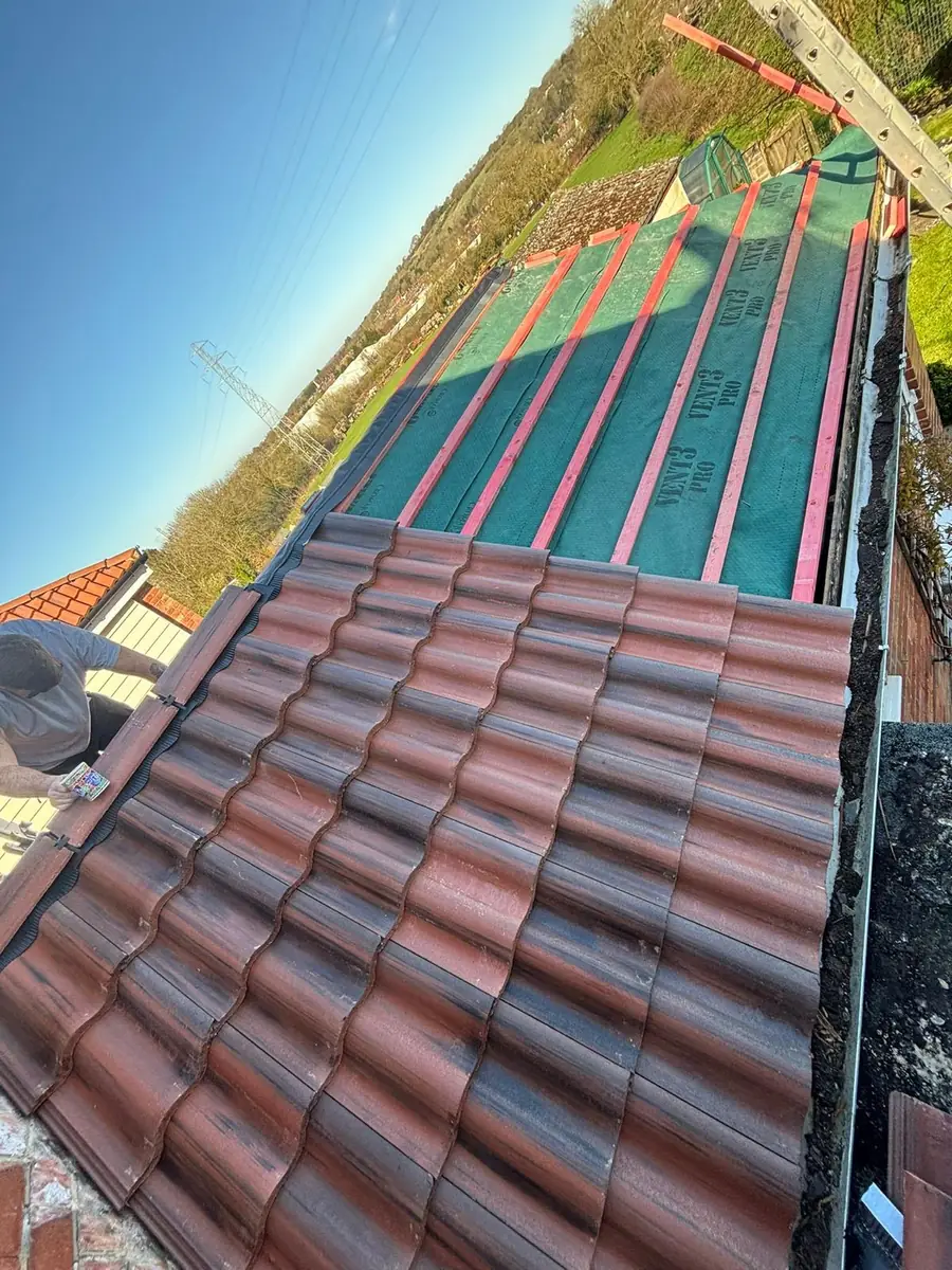 Red interlocking tiles being laid over green membrane and new battens