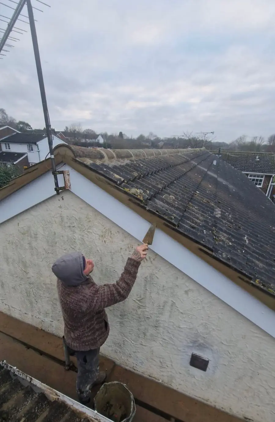 Roofer on a ladder at a gable end working on the fascia and barge board