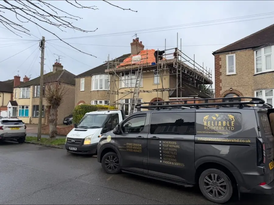 Reliable Roofers van on a Bedfordshire street with the team on a scaffolded roof behind